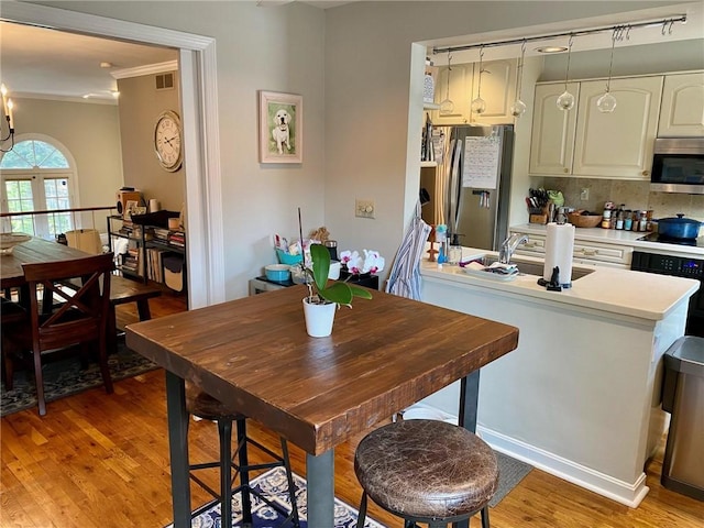 kitchen featuring appliances with stainless steel finishes, crown molding, light wood-style floors, backsplash, and light countertops