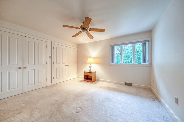 unfurnished bedroom featuring two closets, carpet, baseboards, and ceiling fan