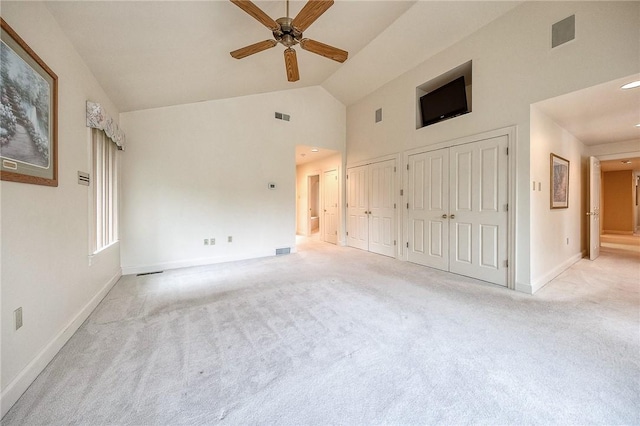unfurnished bedroom featuring two closets, light carpet, baseboards, high vaulted ceiling, and a ceiling fan