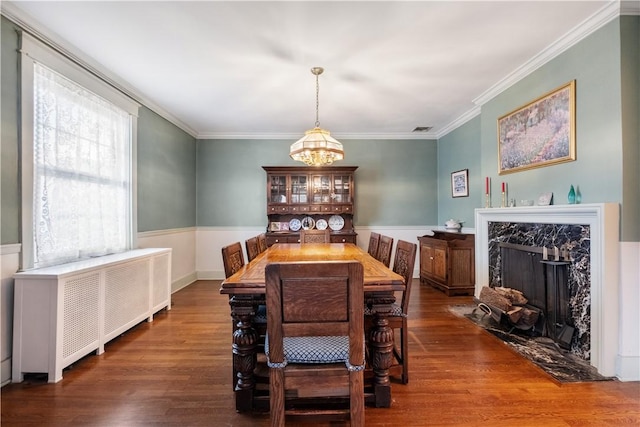 dining area featuring a chandelier, wood finished floors, a fireplace, ornamental molding, and radiator heating unit