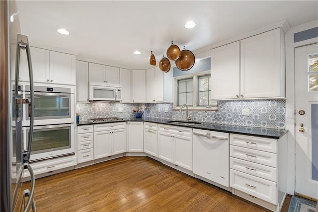 kitchen featuring stainless steel appliances, a sink, dark countertops, wood finished floors, and white cabinetry