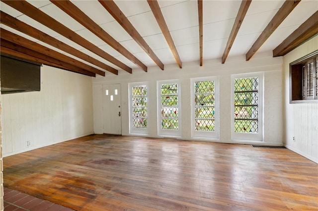 unfurnished living room with plenty of natural light, hardwood / wood-style flooring, beamed ceiling, and wooden walls