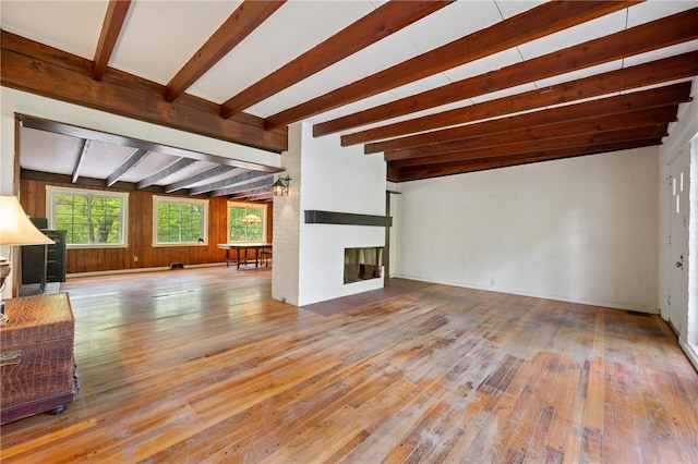 unfurnished living room featuring beamed ceiling, wood-type flooring, and a glass covered fireplace