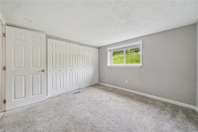 unfurnished bedroom with a textured ceiling, carpet, baseboards, and a closet
