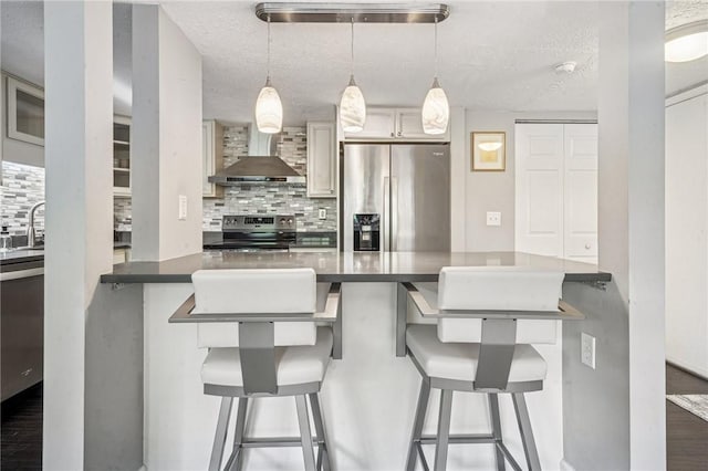 kitchen with wall chimney range hood, appliances with stainless steel finishes, decorative backsplash, a textured ceiling, and a breakfast bar area