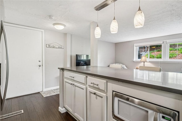 kitchen featuring a textured ceiling, white cabinets, dark wood finished floors, decorative light fixtures, and stainless steel microwave