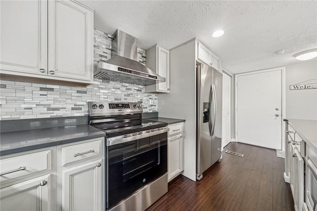 kitchen with stainless steel appliances, wall chimney range hood, a textured ceiling, dark countertops, and dark wood finished floors