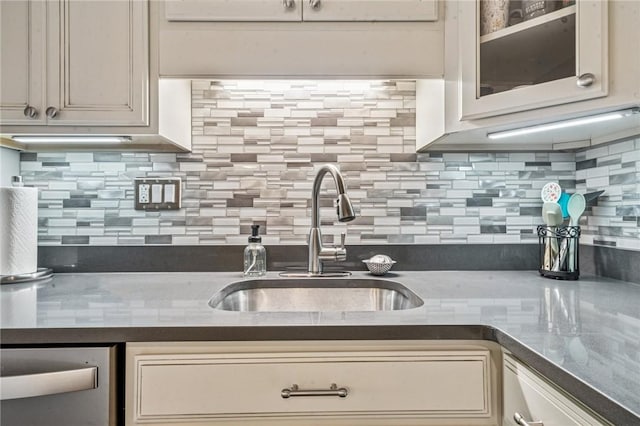kitchen with a sink, backsplash, dark countertops, and glass insert cabinets