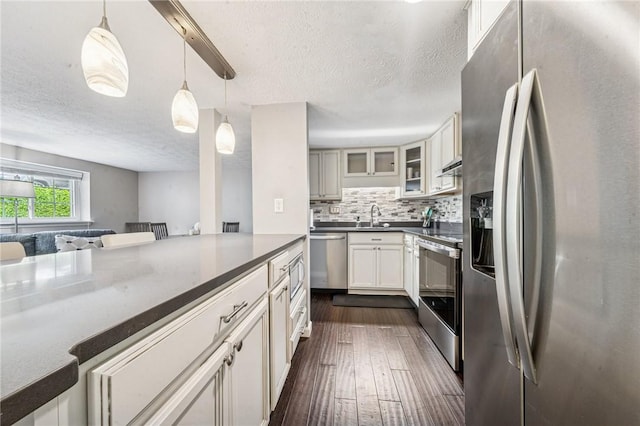 kitchen with appliances with stainless steel finishes, a textured ceiling, dark wood-style floors, tasteful backsplash, and a sink