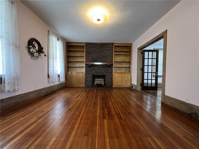 unfurnished living room with dark wood-type flooring, built in features, a brick fireplace, baseboards, and healthy amount of natural light