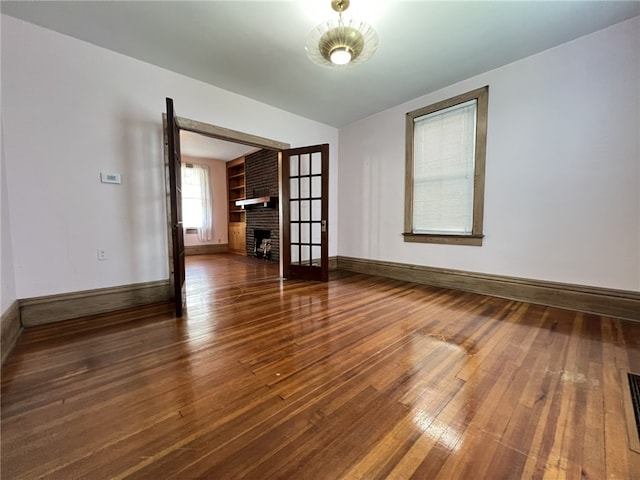 unfurnished living room with wood-type flooring, a brick fireplace, and baseboards