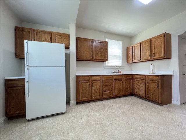 kitchen featuring freestanding refrigerator, brown cabinetry, a sink, and light countertops