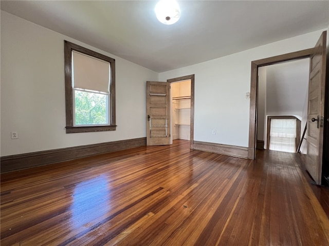 unfurnished bedroom featuring dark wood-type flooring, baseboards, a spacious closet, and a closet