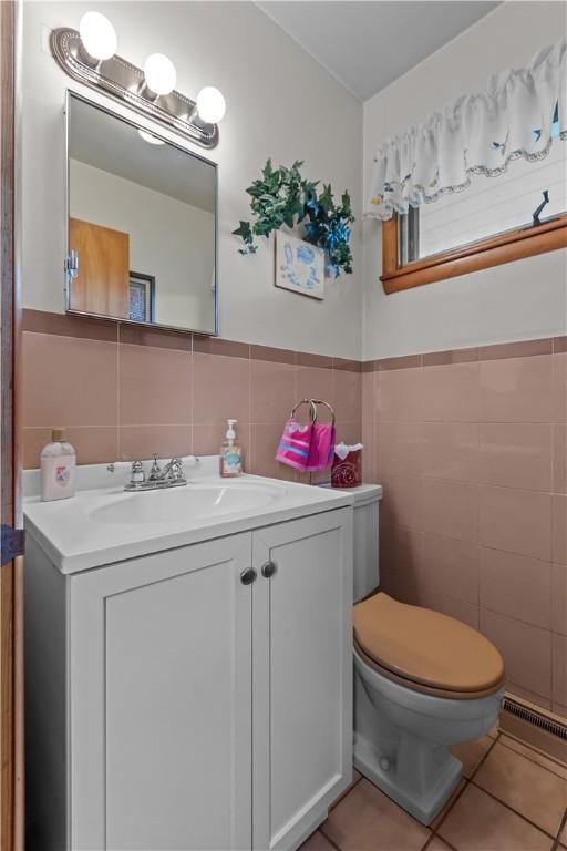 half bathroom with tile walls, tile patterned flooring, vanity, toilet, and wainscoting