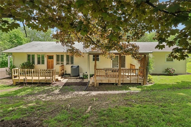 rear view of property with a deck, central air condition unit, and a yard