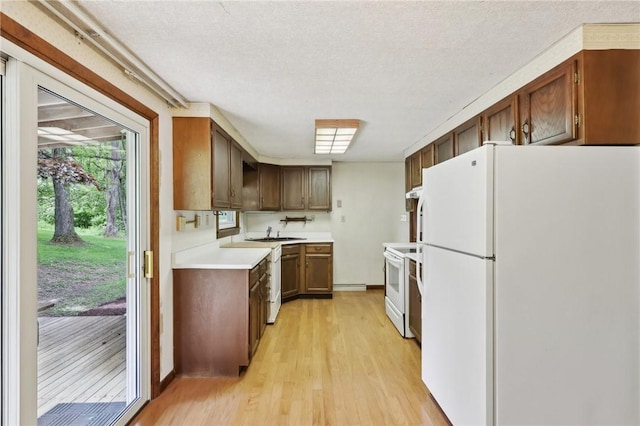 kitchen featuring white appliances, light wood-type flooring, light countertops, a sink, and a textured ceiling