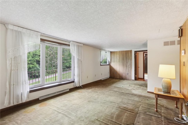 carpeted spare room with a baseboard heating unit, a textured ceiling, and plenty of natural light