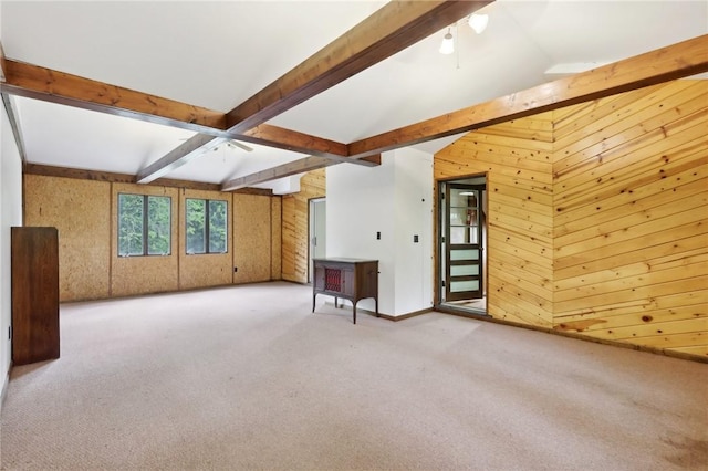 unfurnished living room featuring wood walls, beam ceiling, carpet flooring, and baseboards
