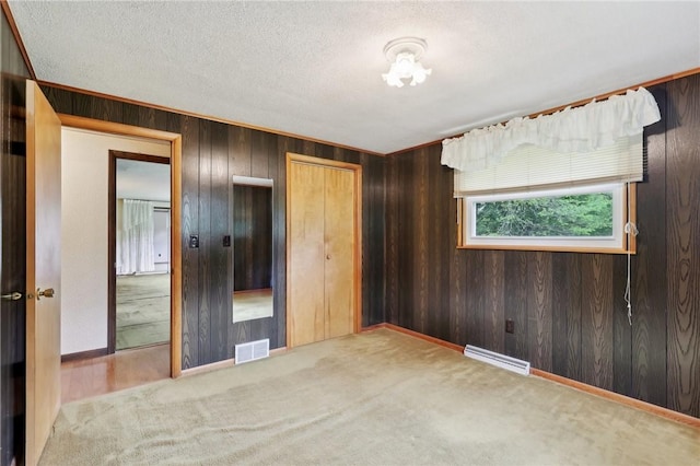 unfurnished bedroom featuring wooden walls, carpet floors, a textured ceiling, and a closet