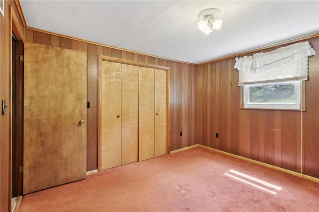 unfurnished bedroom with a closet, wooden walls, and carpet floors