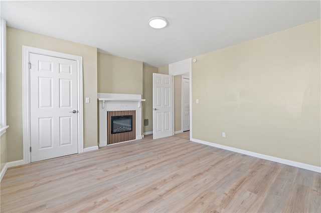 unfurnished living room with light wood-style flooring, a glass covered fireplace, and baseboards