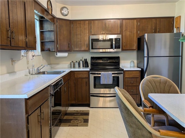kitchen with appliances with stainless steel finishes, open shelves, a sink, and light countertops