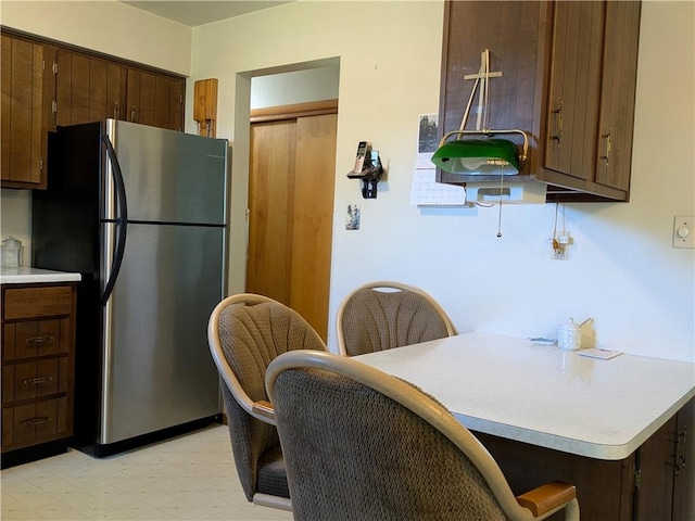 kitchen featuring freestanding refrigerator, light floors, light countertops, dark brown cabinets, and a peninsula