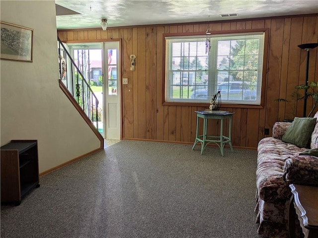 carpeted living room featuring baseboards, wooden walls, and stairs