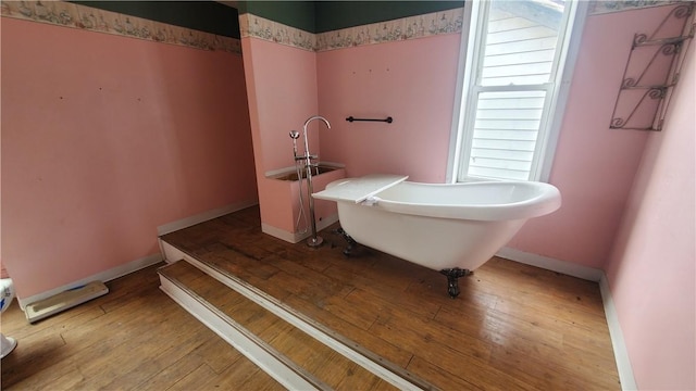 full bath featuring a freestanding tub, hardwood / wood-style flooring, and baseboards
