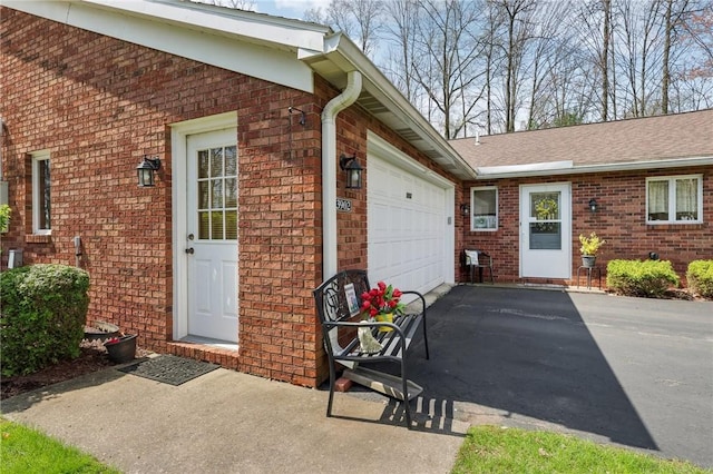 view of exterior entry featuring brick siding, an attached garage, and driveway