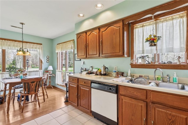 kitchen featuring white dishwasher, light countertops, a sink, brown cabinetry, and decorative light fixtures