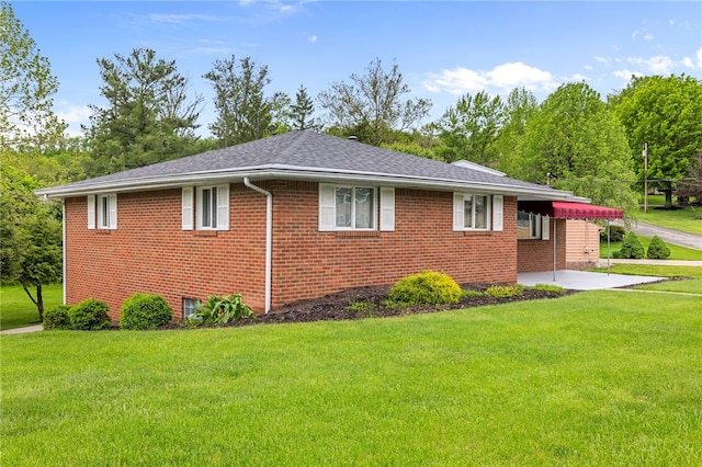 view of side of property featuring a yard, brick siding, a patio area, and a shingled roof