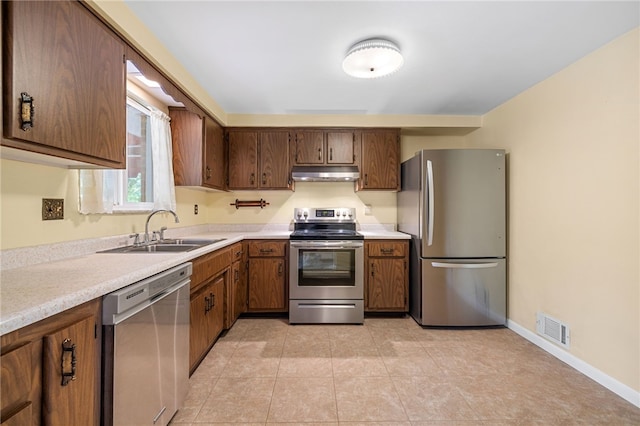 kitchen featuring stainless steel appliances, under cabinet range hood, a sink, light countertops, and brown cabinets