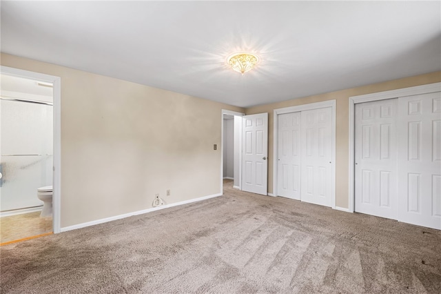 unfurnished bedroom featuring carpet floors, two closets, ensuite bathroom, and baseboards