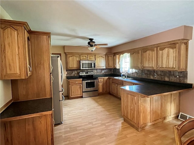 kitchen featuring stainless steel appliances, a peninsula, a sink, decorative backsplash, and ceiling fan