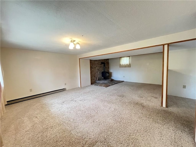 unfurnished living room featuring a baseboard heating unit, a wood stove, carpet flooring, and a textured ceiling