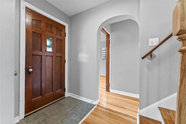 entrance foyer featuring arched walkways, baseboards, and dark wood-style floors