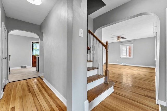 stairway with ceiling fan, arched walkways, hardwood / wood-style floors, and baseboards