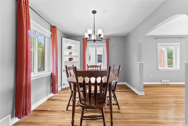 dining area featuring arched walkways, a chandelier, light wood-style flooring, and plenty of natural light