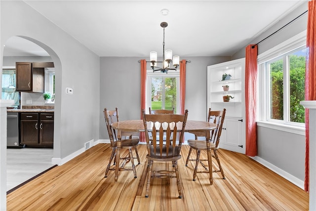 dining room with arched walkways, light wood-style floors, and healthy amount of natural light