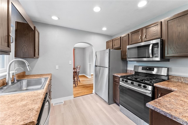 kitchen featuring stainless steel appliances, a sink, arched walkways, dark brown cabinets, and recessed lighting