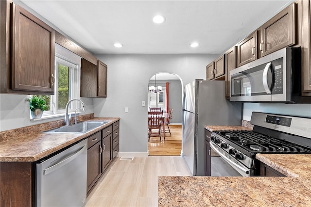 kitchen featuring appliances with stainless steel finishes, a sink, arched walkways, light wood-style flooring, and dark brown cabinetry