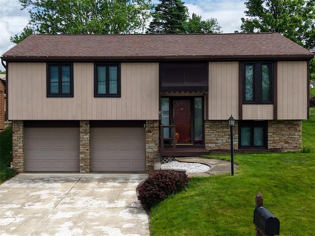 split foyer home featuring an attached garage, stone siding, a front lawn, concrete driveway, and roof with shingles