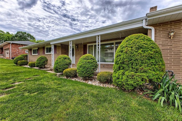 view of front of property featuring brick siding, a front yard, a chimney, and a porch