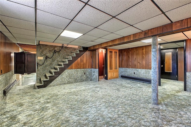 finished basement with carpet, wood walls, stairs, and a paneled ceiling