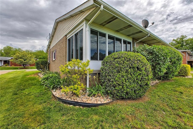 view of property exterior with brick siding, a lawn, and a sunroom