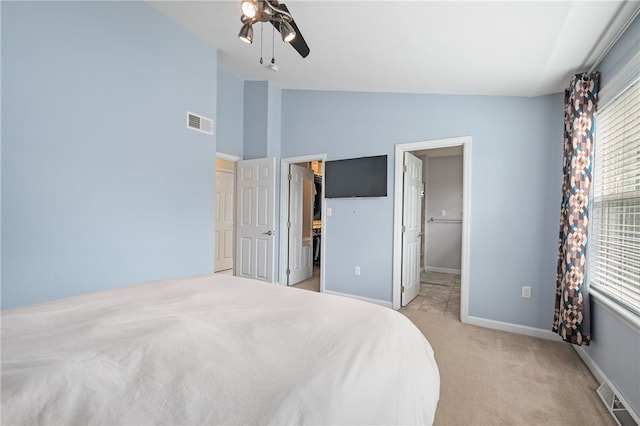 bedroom featuring vaulted ceiling, multiple windows, light carpet, baseboards, and a walk in closet