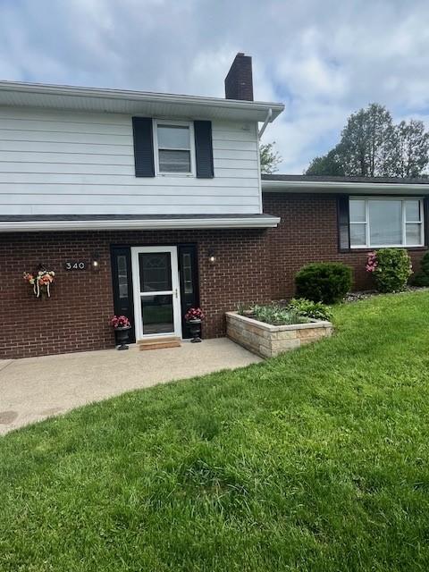 view of front of home featuring a chimney, a front yard, and brick siding