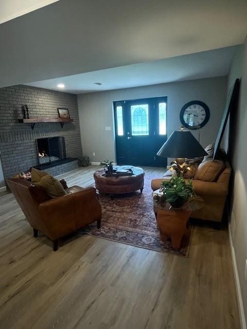 living room with wood finished floors, baseboards, and a brick fireplace