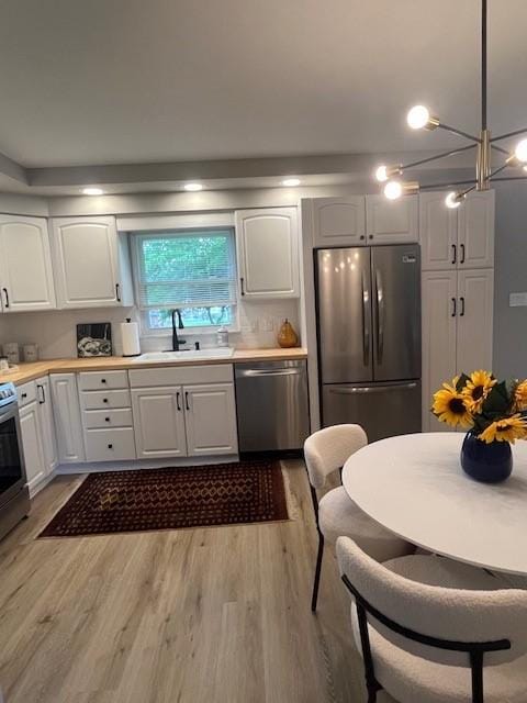kitchen featuring stainless steel appliances, light wood finished floors, white cabinetry, a sink, and light countertops